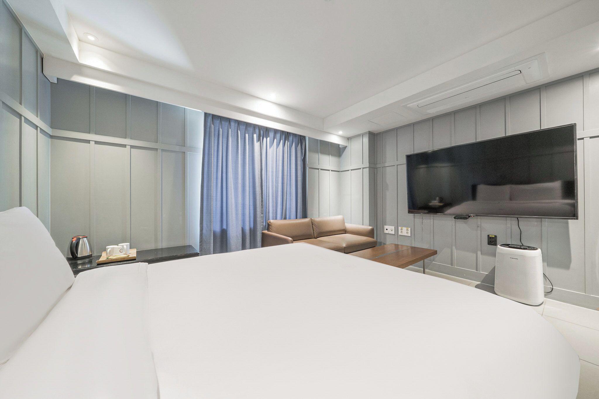 Une chambre d’hôtel moderne dotée d’un grand lit, d’un canapé, d’un téléviseur à écran plat fixé au mur et d’une machine à café sur la table de chevet.