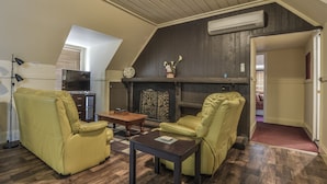 A loft-style living room with a fireplace, wooden flooring, and a television. - Gold Mine Guesthouse (Nundle)