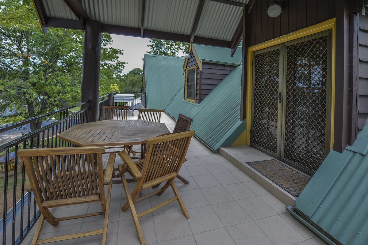 Un espace extérieur abrité, doté d’une table et de chaises en bois, d’une rambarde en métal et d’une porte munie d’un moustiquaire.