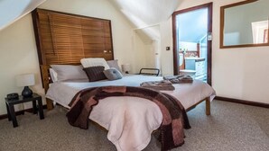 A bedroom with a sloped ceiling, a bed with a headboard, a bedside table with a lamp, and a large mirror on the wall. - Gold Mine Guesthouse (Nundle)