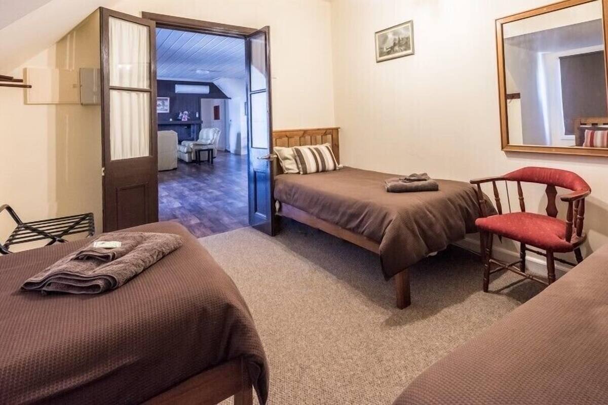 Une chambre avec deux lits, une chaise, un miroir et une porte donnant sur un couloir.