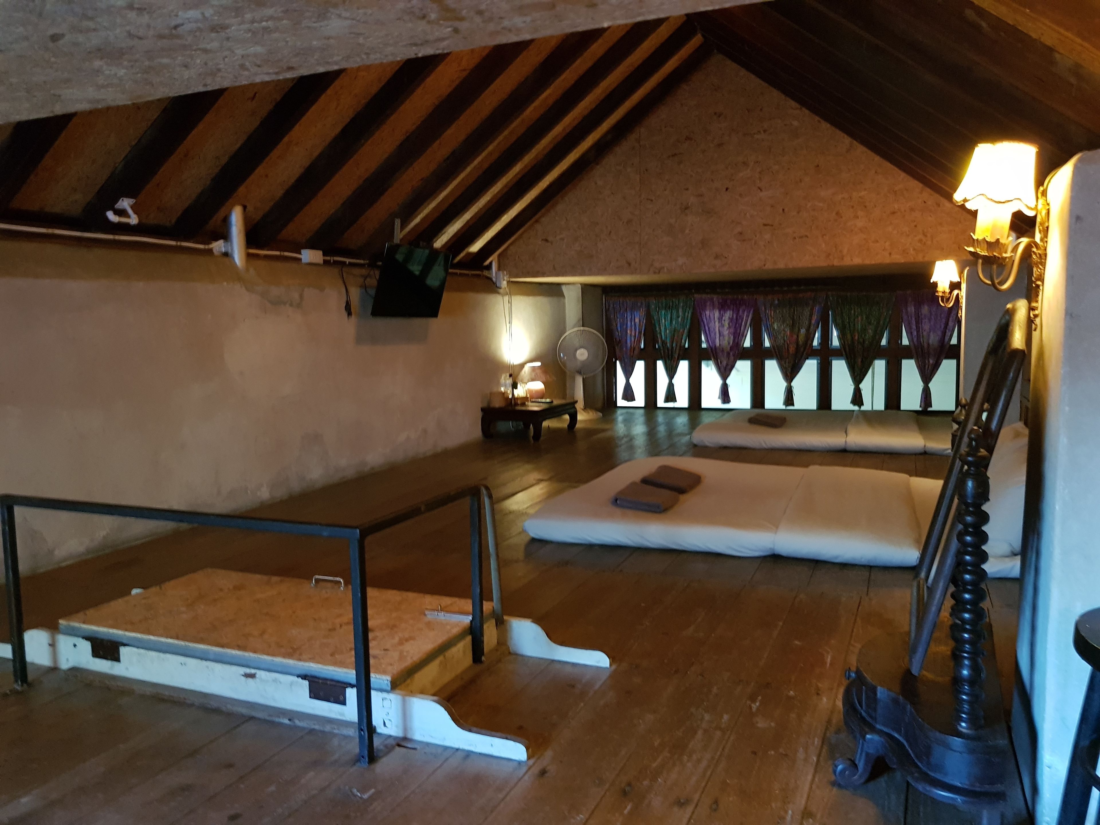 Una habitación en el ático con vigas de madera, un sofá, una mesita con una lámpara y un ventilador.
