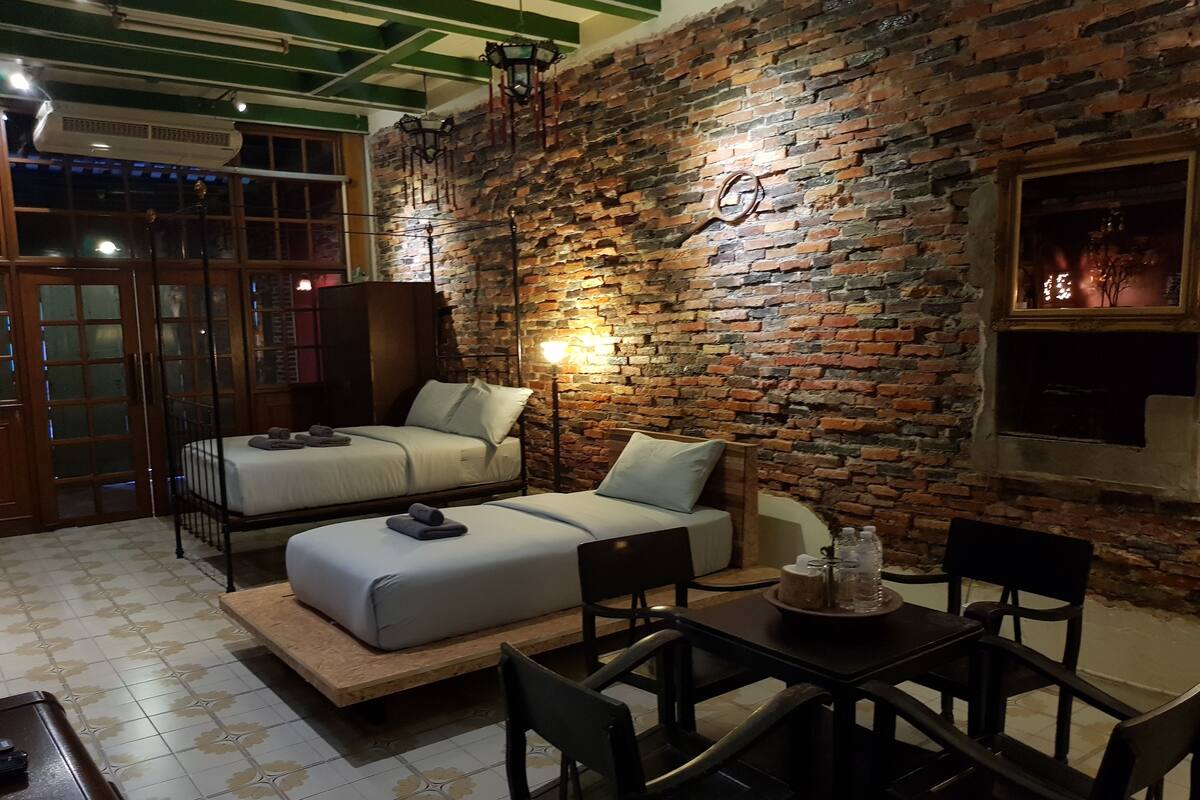 Um quarto aconchegante com duas camas, uma mesa de jantar e uma parede de tijolos.