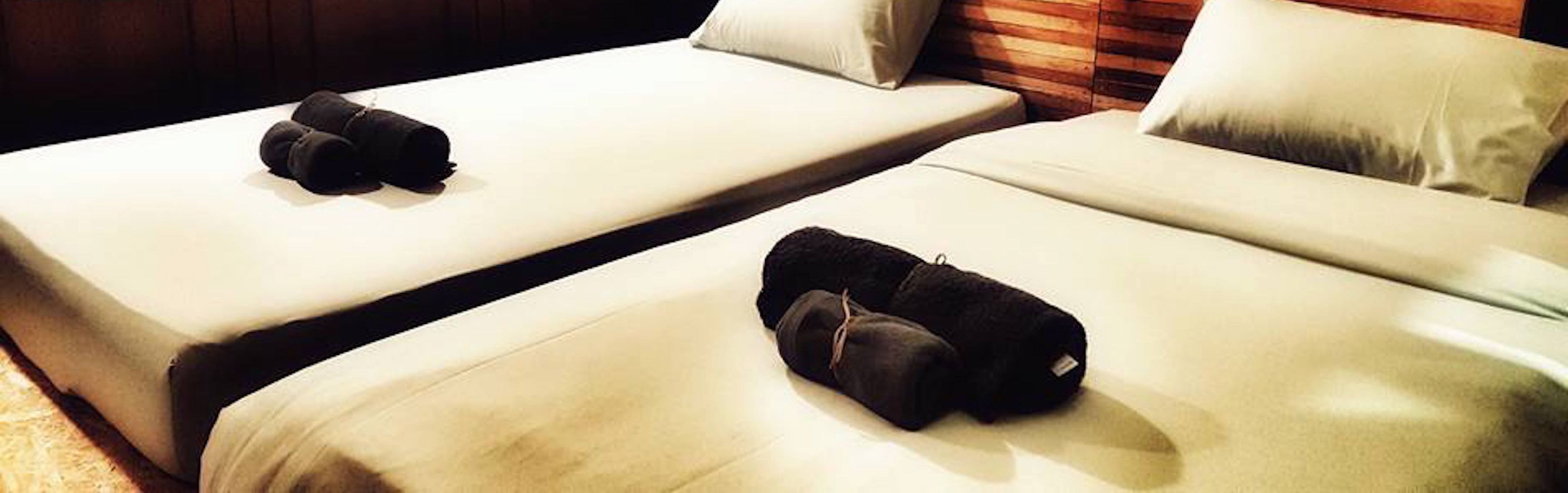 Two single beds with white linens and black towels, a wooden headboard, and a light-colored carpet.