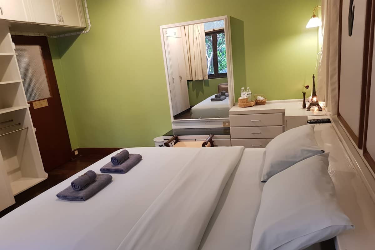 Quarto de hotel com cama, escrivaninha, espelho e guarda-roupa.
