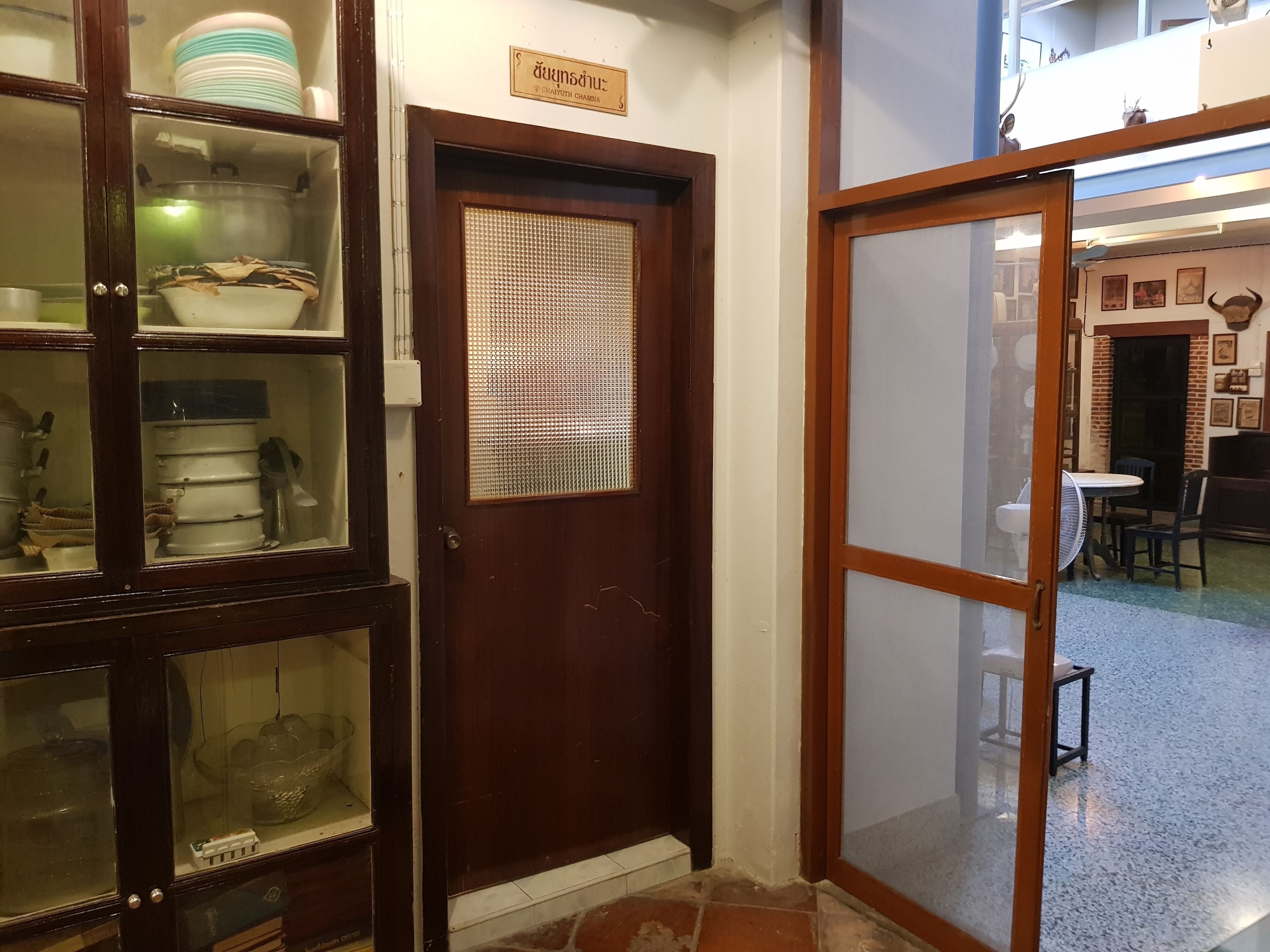 A traditional wooden door with a sign above it, leading to a room with a tiled floor and a dining area visible through the door.