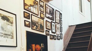 A staircase with a wooden handrail and a wall with multiple framed photographs and a shelf with pottery. - The Roo Classic Hometel (Songkhla)