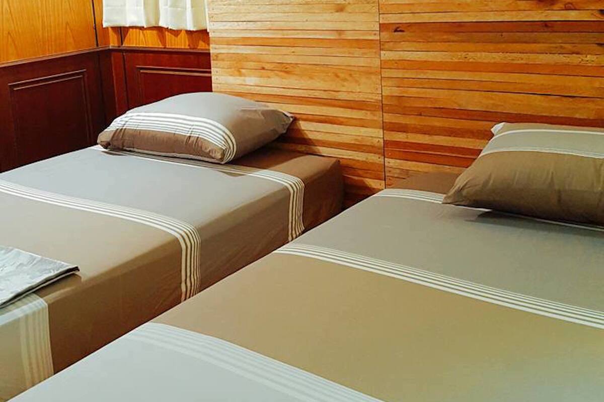 Quarto de hotel com duas camas, cabeceiras de madeira e uma janela com cortinas.