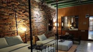 A hotel room with a brick wall, a bed with a metal frame, a sofa, a small table, and a mirror. - The Roo Classic Hometel (Songkhla)