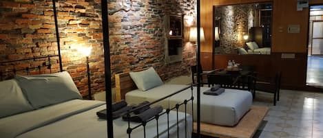 A hotel room with a brick wall, a bed with a metal frame, a sofa, a small table, and a mirror.