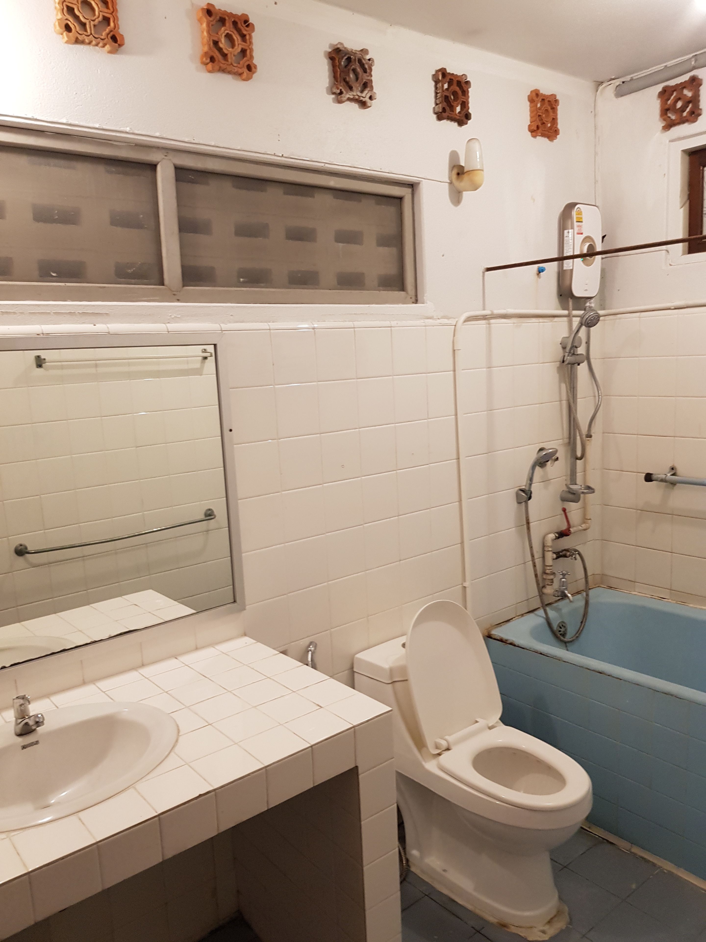Un baño con azulejos blancos, un lavamanos, un inodoro, una ducha y elementos decorativos en la pared.
