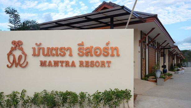 A sign for Mantra Resort with a modern design and a row of buildings in the background. - Mantra Resort (Songkhla)