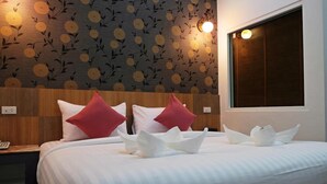 A hotel room with a large bed, two red pillows, a wooden headboard, and a floral wallpaper design. - Mantra Resort (Songkhla)