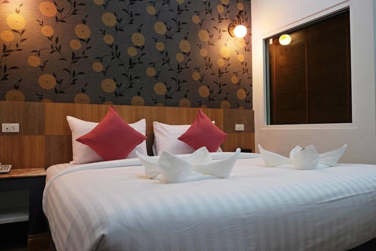 A hotel room with a large bed, two red pillows, a wooden headboard, and a floral wallpaper design.