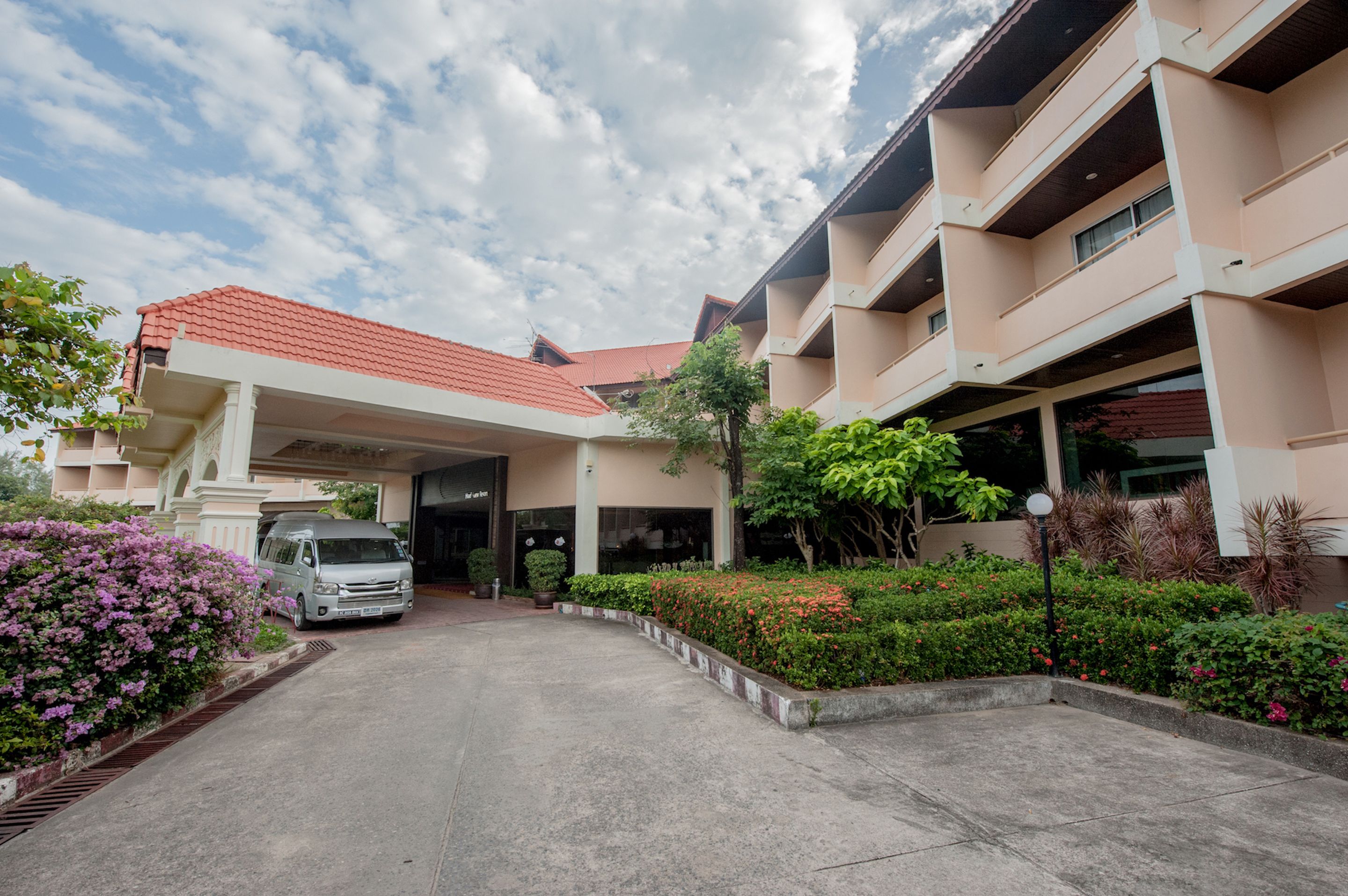 A hotel entrance with a covered driveway, a parked van, and a well-maintained garden with various plants and flowers.