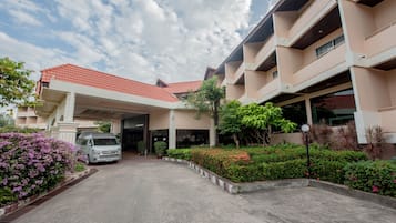 A hotel entrance with a covered driveway, a parked van, and a well-maintained garden with various plants and flowers.