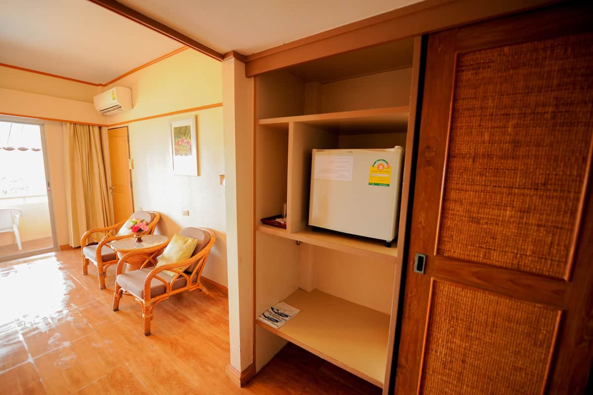A room with a wooden door, a white refrigerator, wicker chairs, and a small table with a cushion.