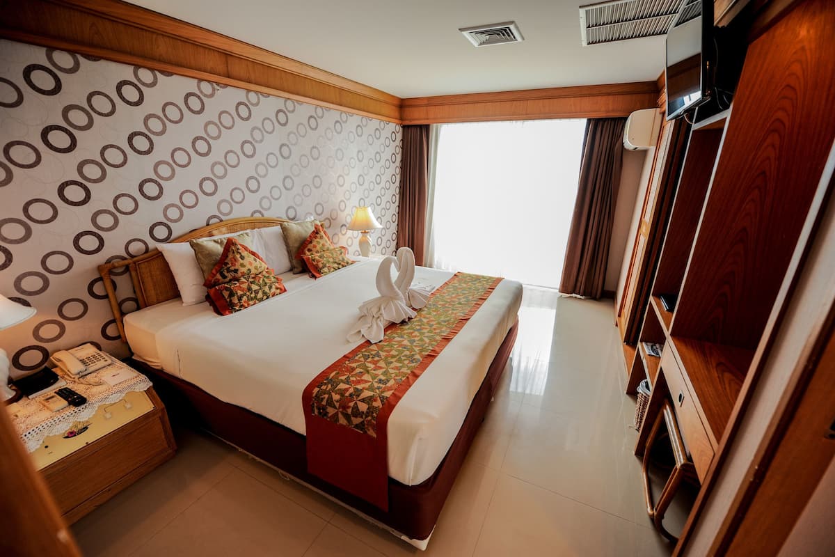 A hotel room with a large bed, a wooden headboard, a bedside table with a lamp, and a TV mounted on the wall.