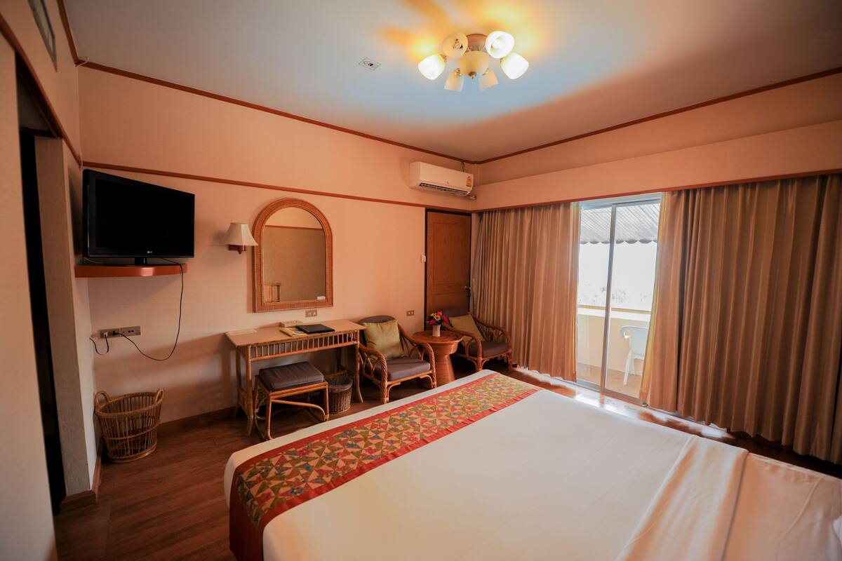 A hotel room with a large bed, a desk with a chair, a television, and a window with curtains.