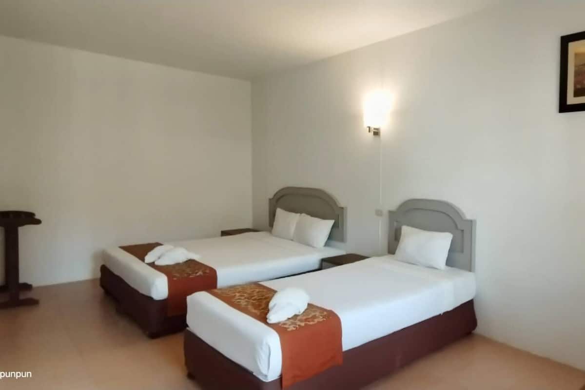 A hotel room with two beds, a small table, a chair, and a framed picture on the wall.