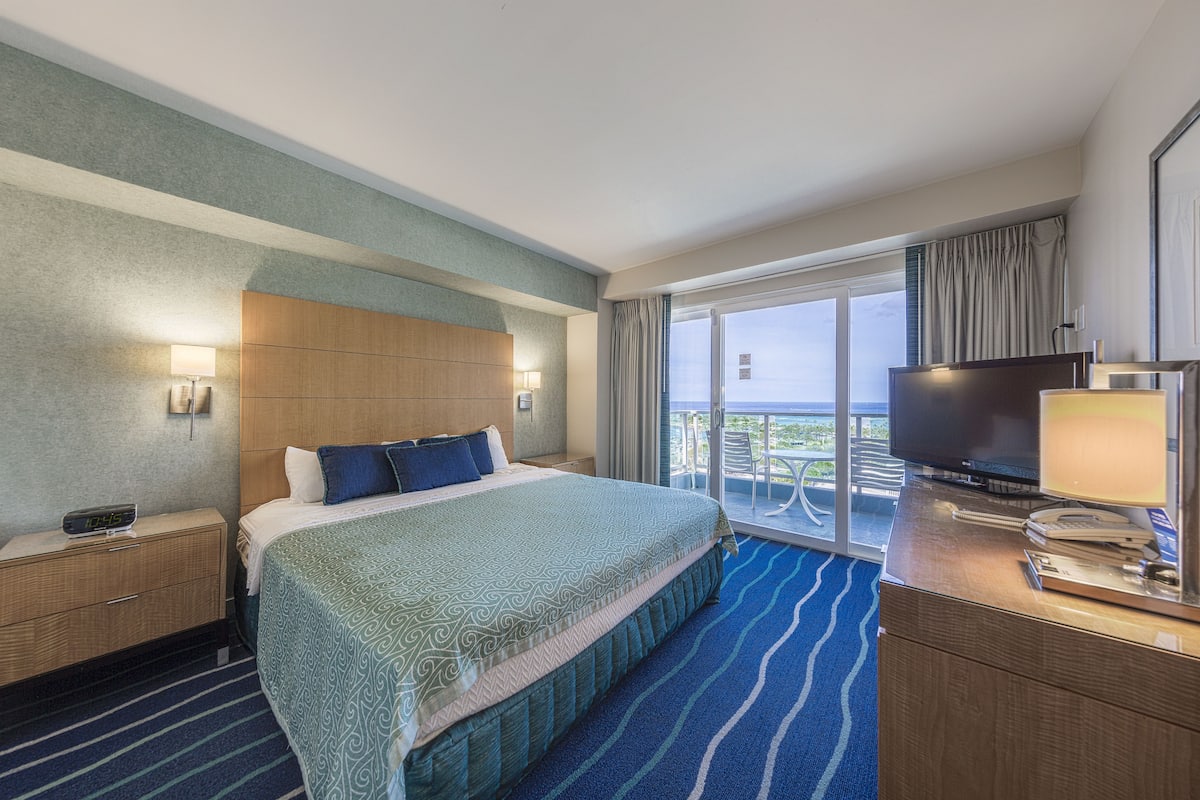 Une chambre d’hôtel avec un grand lit, une télévision, un bureau avec une lampe et un balcon avec vue.