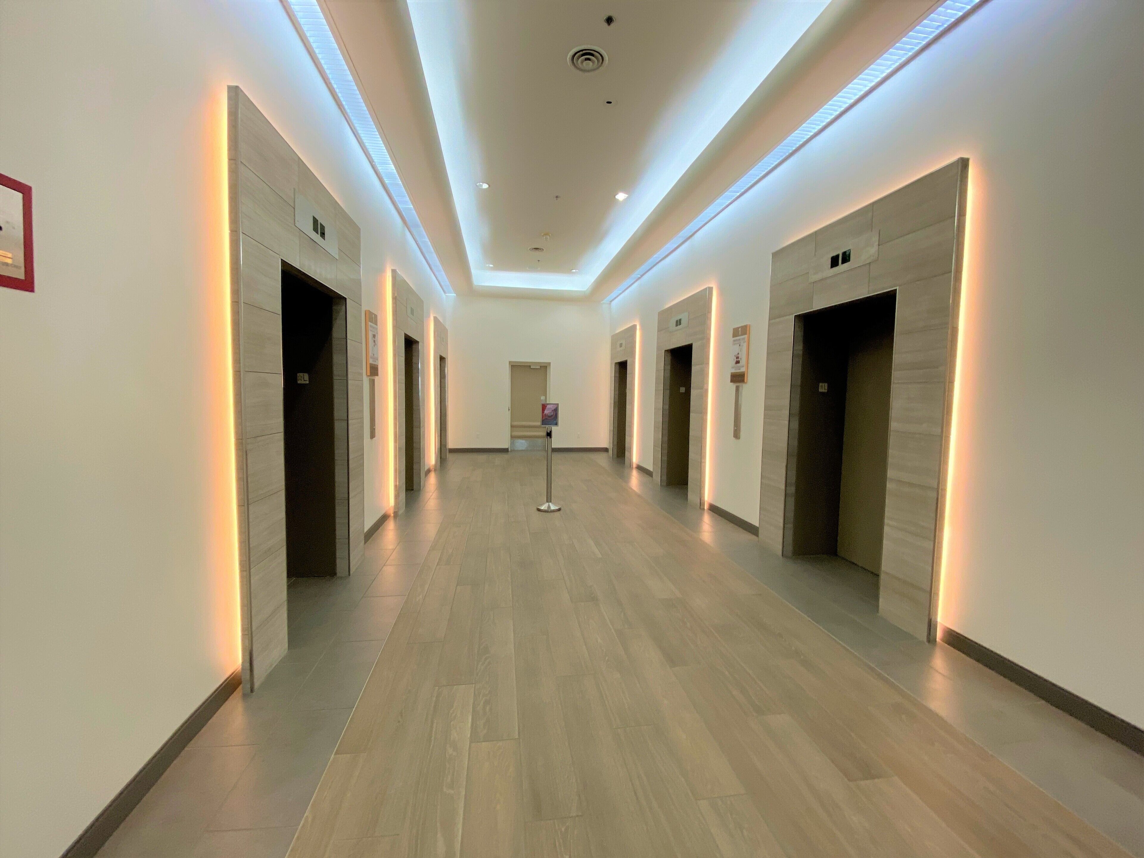 A modern hotel corridor with wooden flooring, recessed lighting, and multiple doors likely leading to rooms or amenities.
