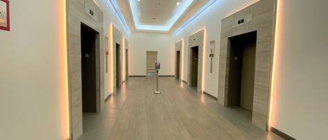A modern hotel corridor with wooden flooring, recessed lighting, and multiple doors likely leading to rooms or amenities.