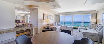 A modern hotel room with a dining area, a sofa set, and a view of the ocean.