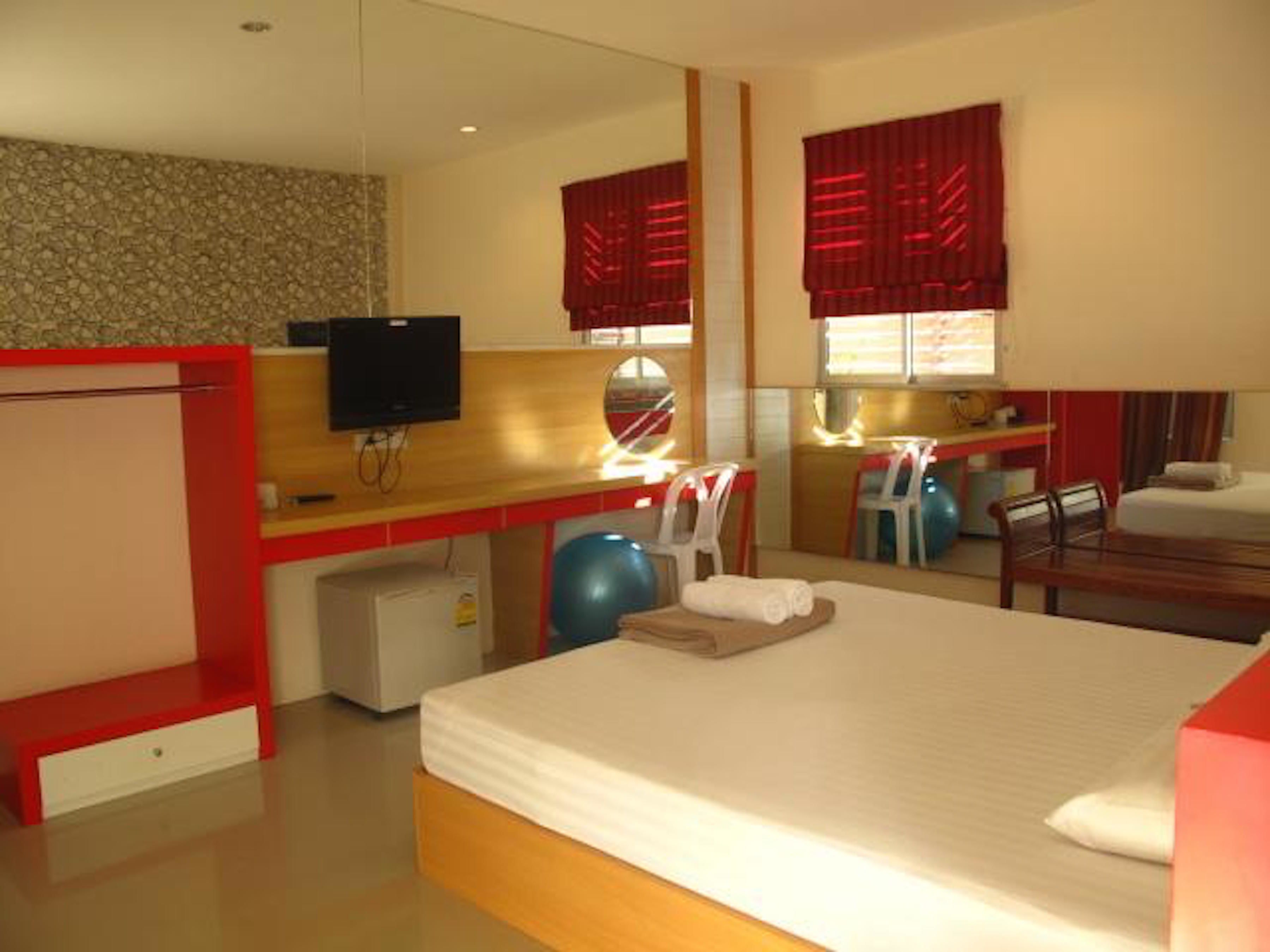 A hotel room with a bed, a desk, a television, a small refrigerator, and a window with red curtains.