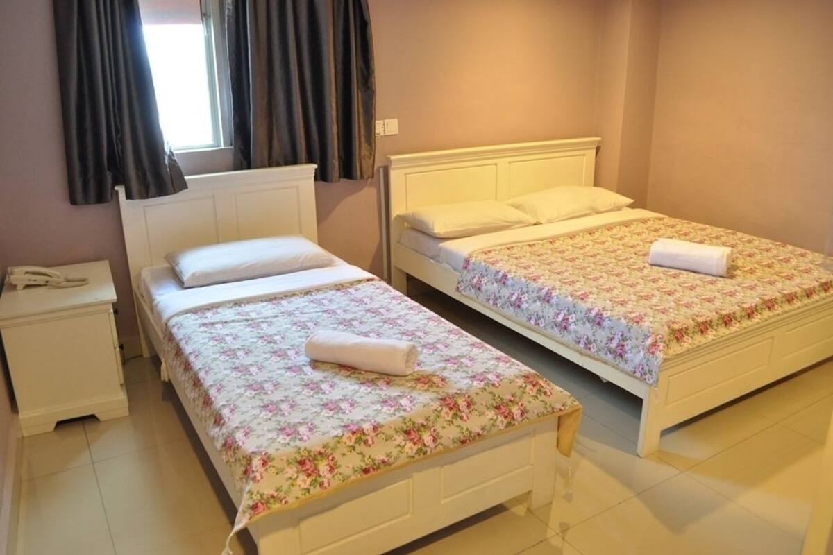 Habitación con dos camas individuales, cada una con una colcha estampada y una toalla enrollada. Se observa una mesita de noche con un teléfono y una ventana con cortinas.