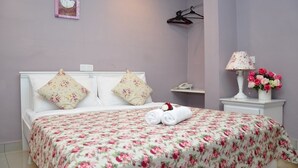 A neatly made bed with floral bedding, a bedside lamp, and a vase of flowers. - Hotel KK Equine Park (Seri Kembangan)