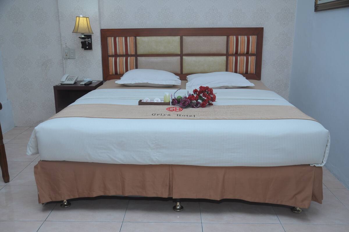 A hotel room with a large bed, a nightstand with a lamp, a telephone, and a tray with toiletries.