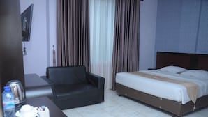 A hotel room with a bed, a sofa, a TV, and a coffee table with cups and a water bottle. - Griya Hotel (Medan)