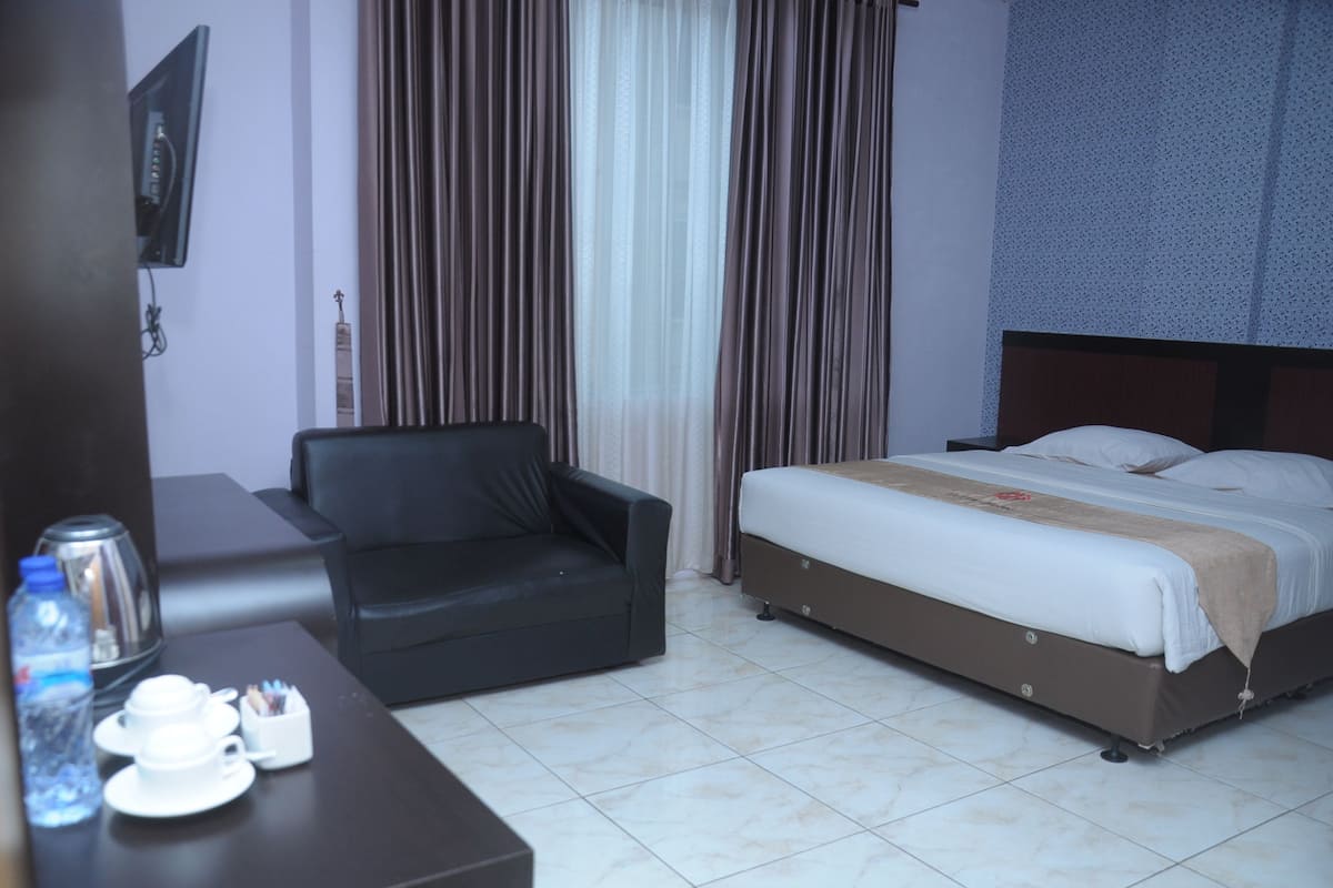 A hotel room with a bed, a sofa, a TV, and a coffee table with cups and a water bottle.