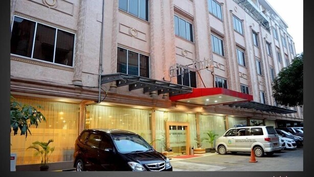 A multi-story hotel with a classic architectural design, featuring a prominent entrance with a red awning and a glass facade. - Griya Hotel (Medan)
