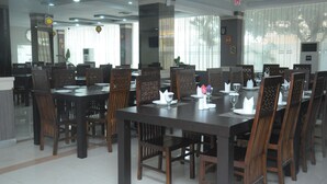 A dining area with multiple tables and chairs, large windows with blinds, and ceiling-mounted lights. - Griya Hotel (Medan)