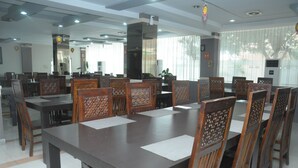 A conference room with a long table and wooden chairs, large windows with curtains, and ceiling lights. - Griya Hotel (Medan)