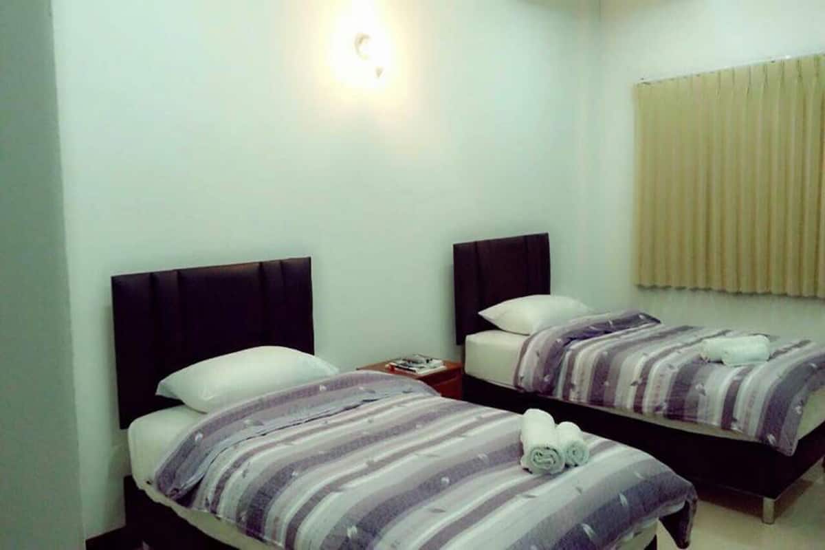 Habitación de hotel con dos camas, cada una con cubrecama y almohadas a rayas. Entre las camas, una mesita de noche con una lámpara y un libro.