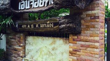 Entrada de um edifício com uma grande estrutura semelhante a uma rocha, uma estátua de leão dourado e uma placa com texto em tailandês.