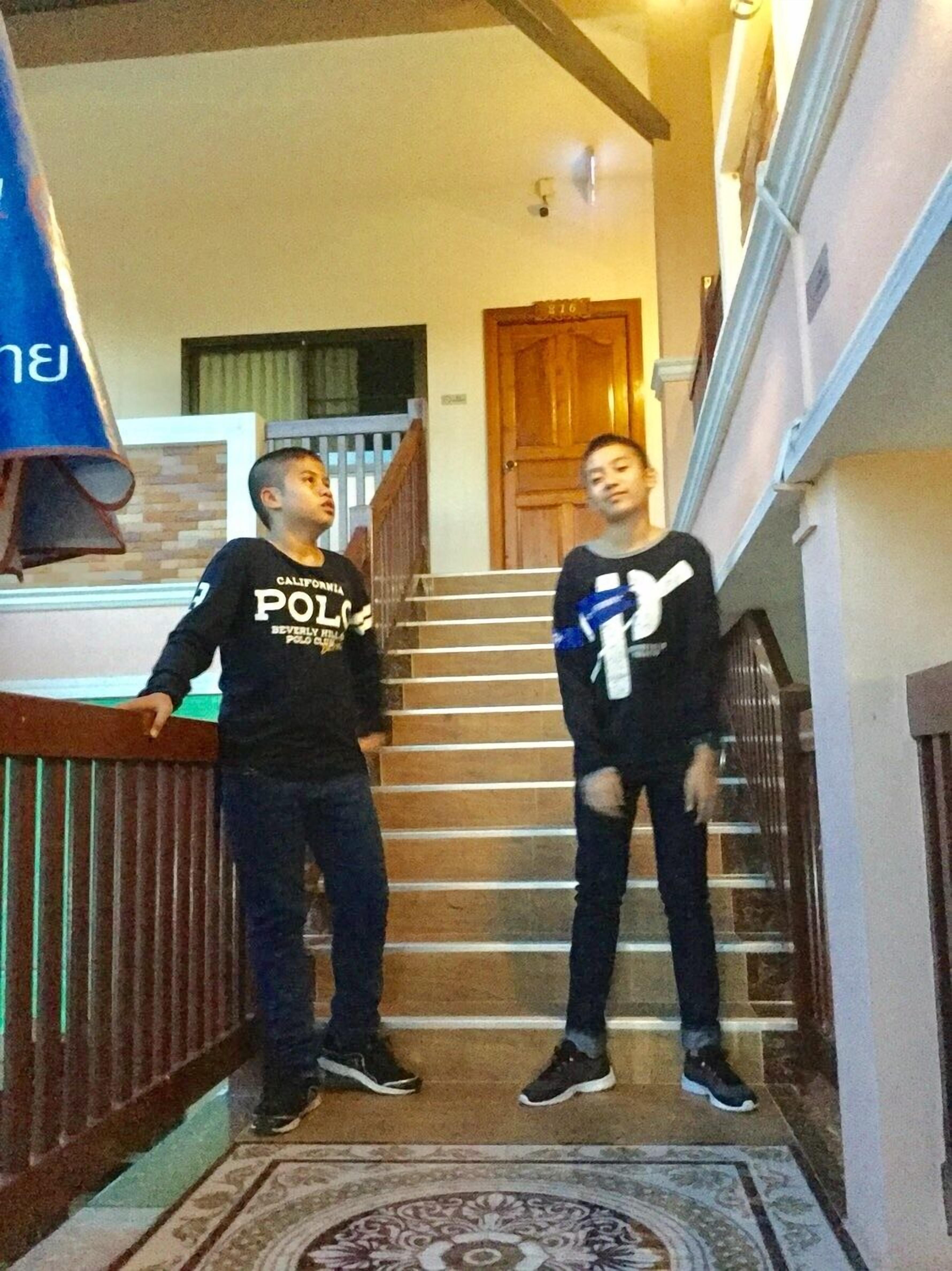 Twee personen staan op een trap met een patroonrijk tapijt en een houten leuning.