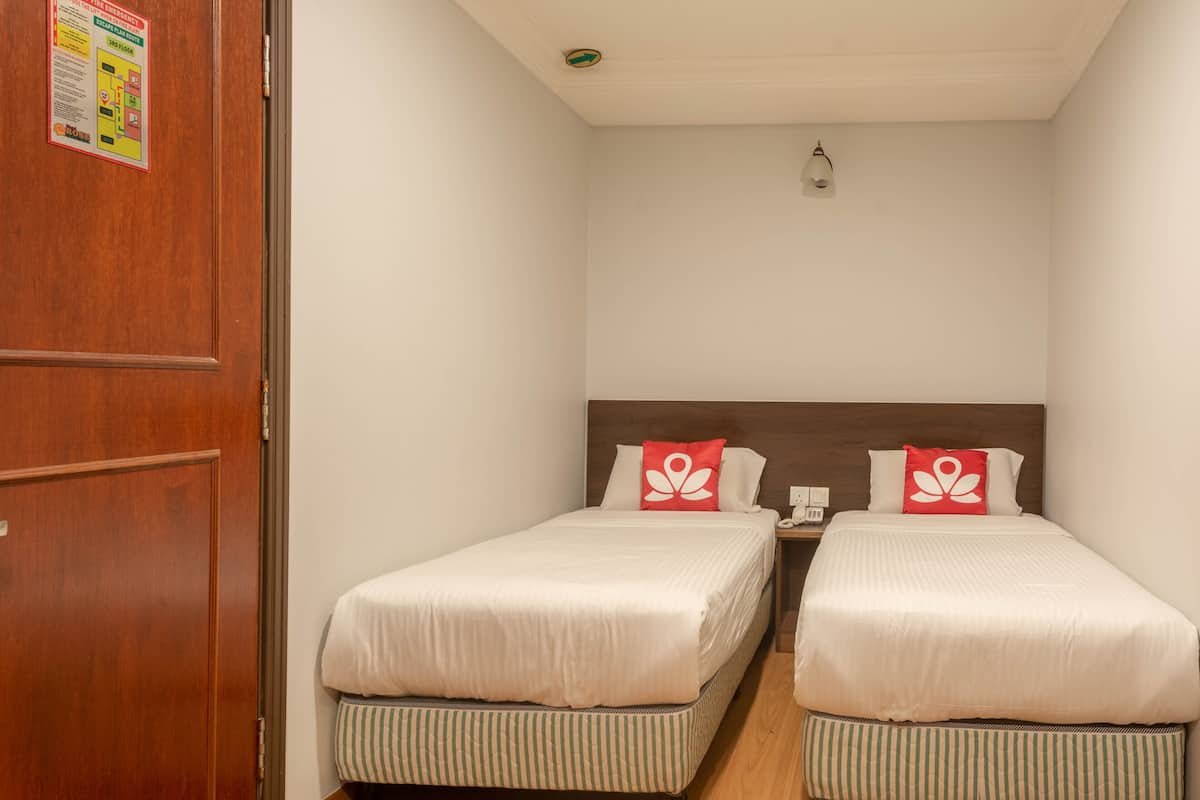 A small, clean room with two single beds, a wooden door, and a nightstand with a phone.