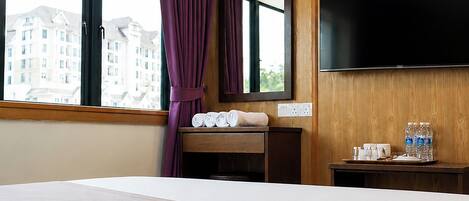 Una habitación de hotel con una cama grande, un televisor de pantalla plana montado en la pared, una ventana con cortinas moradas y vistas a edificios.