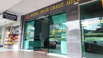 Exterior do Hotel Rose Crest Hill, com entrada visível, placa de identificação acima da entrada e carro estacionado em frente.
