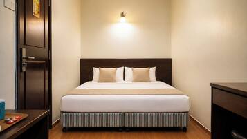 A hotel room with a bed, bedside tables, a nightstand, a lamp, and a door.
