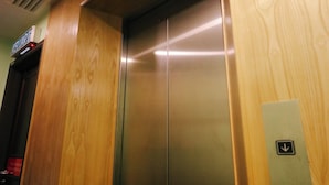 Een lift met een houten paneelafwerking en een digitaal scherm boven de deur.