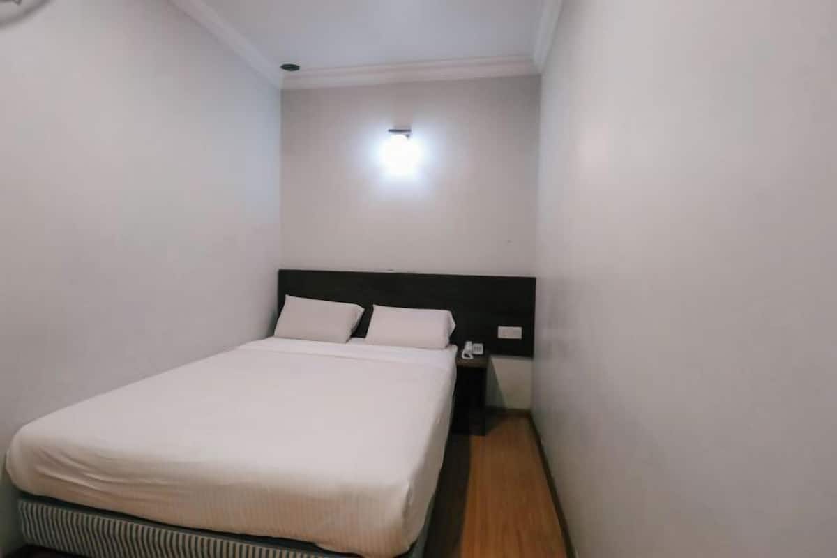 A small, neatly made bed in a room with white walls and a wooden floor.