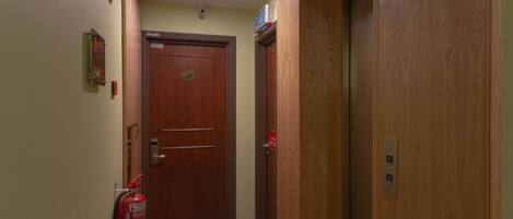 A hallway with a wooden door, a fire extinguisher, and a sign above the door.