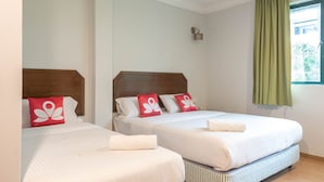Hotelkamer met twee bedden, elk met witte lakens en rode kussens, een houten hoofdbord, een klein wandlampje en een raam met groene gordijnen.