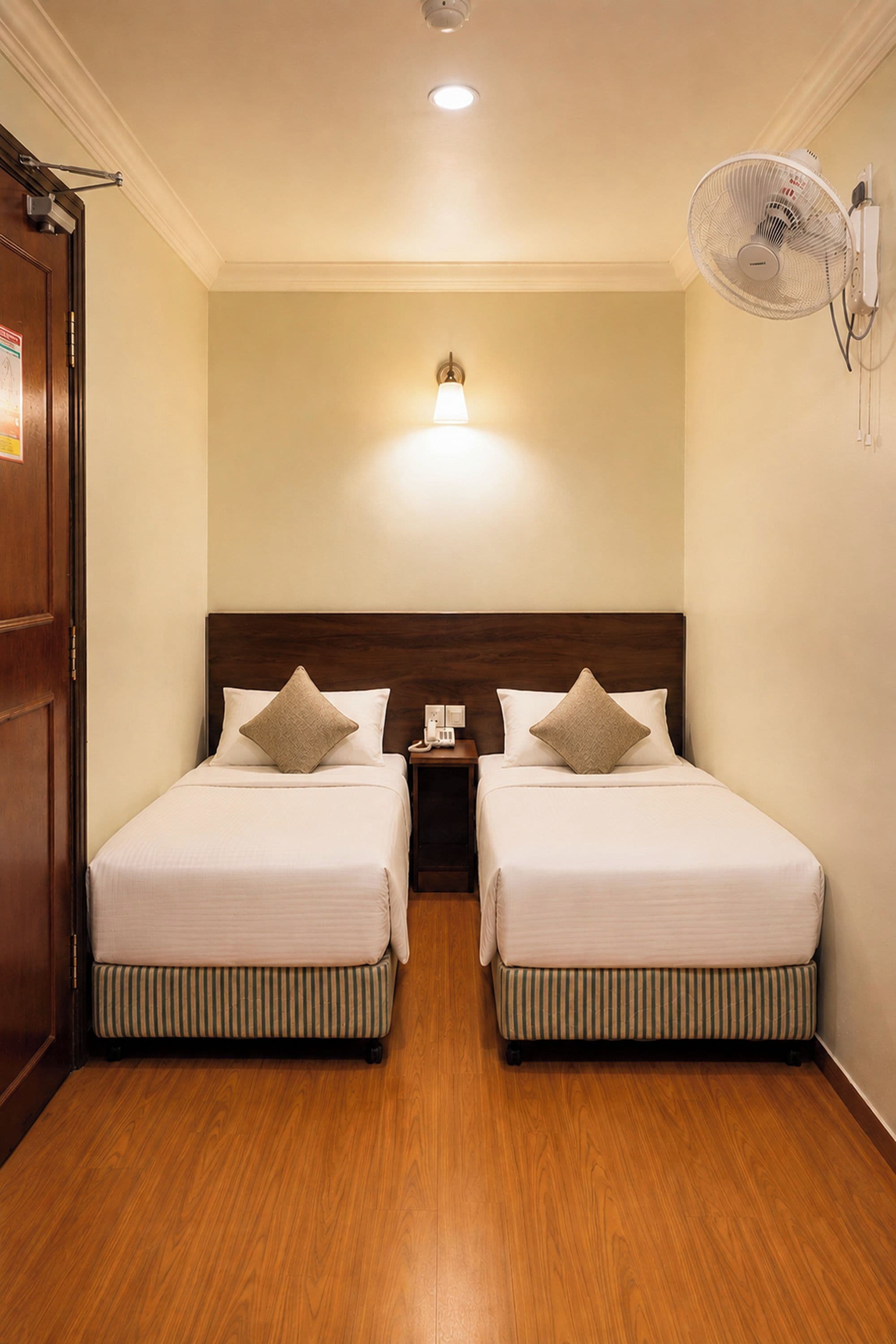 A hotel room with two beds, a nightstand, a wall-mounted fan, and a ceiling light.