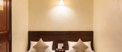 A hotel room with two beds, a nightstand, a wall-mounted fan, and a ceiling light.